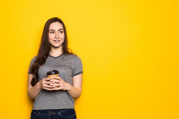 Young woman holding cup with tea or coffee on yellow wall. Lifestyle and food concept. Close up.