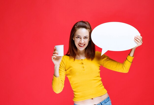 Young woman holding a disposable cup of drink and an ovale info board