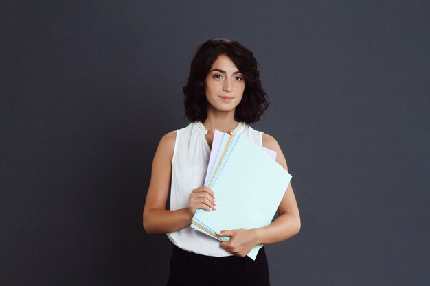 Young woman holding documents in hands over grey wall