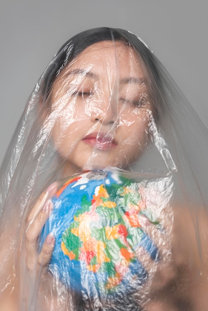 Young woman holding an earth globe while being covered in plastic