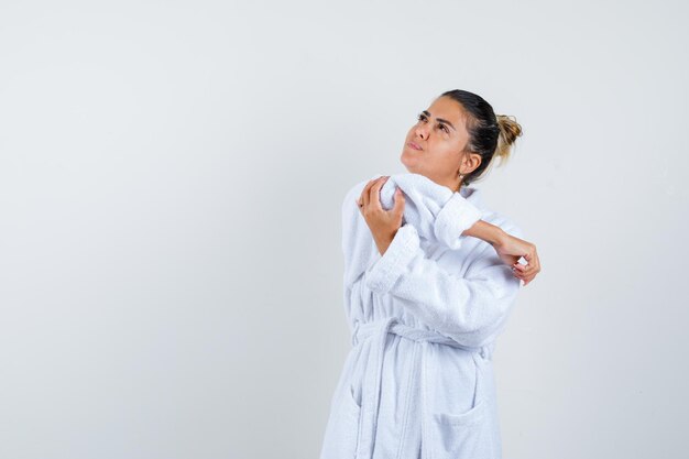 Young woman holding elbow in bathrobe and looking thoughtful