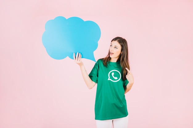 young woman holding empty blue speech bubble over pink background