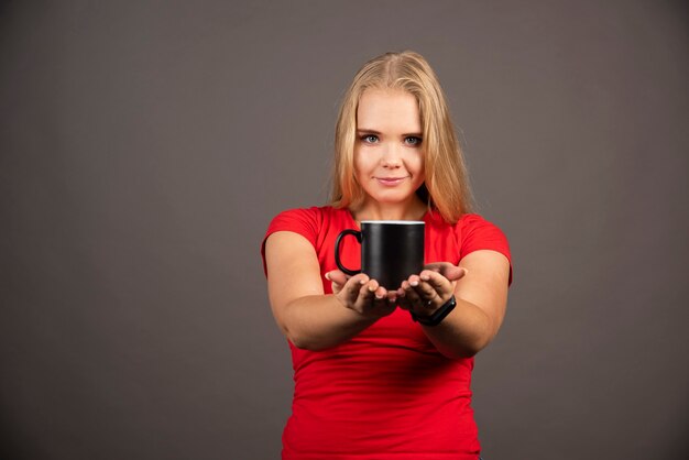 Молодая женщина, держащая пустую чашку на черной стене.