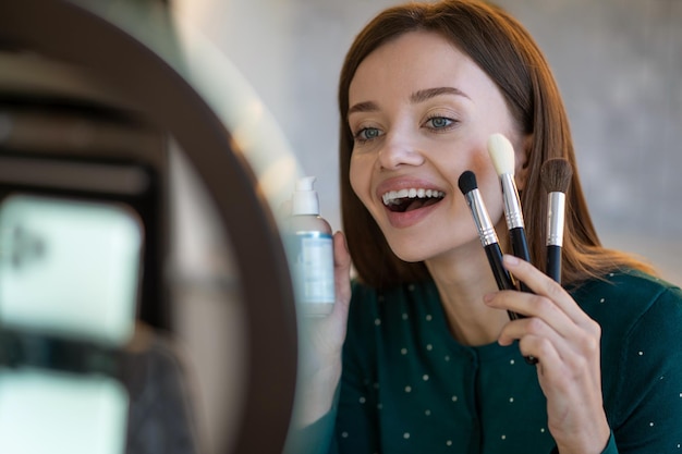 Free photo young woman holding face brushes and smiling