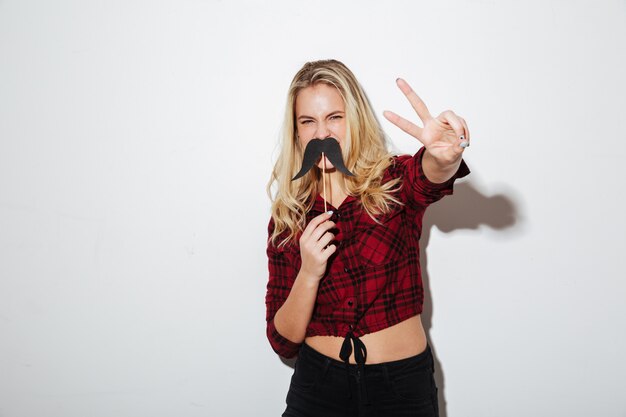 Young woman holding fake moustache showing peace gesture.