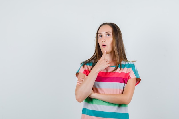 Молодая женщина держит палец на подбородке в футболке и смотрит задумчиво. передний план.