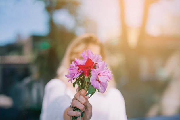 Foto gratuita mazzo del fiore della tenuta della giovane donna davanti al suo fronte contro il contesto vago