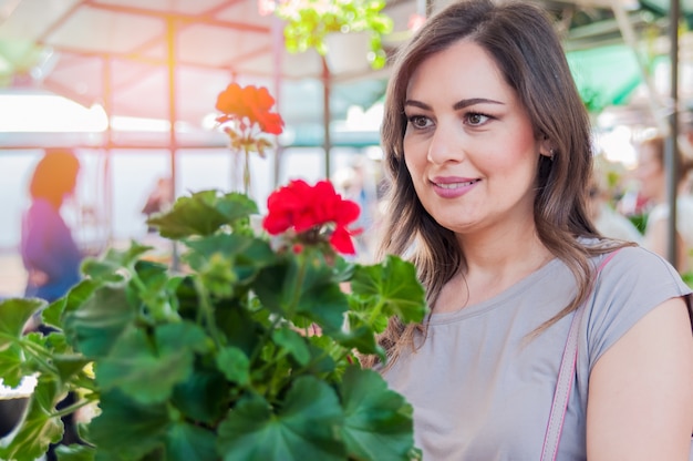 ガーデニングセンターで粘土ポットにゼラニウムを保持している若い女性。ガーデニング、植え付け - ゼラニウムの花を持つ女性