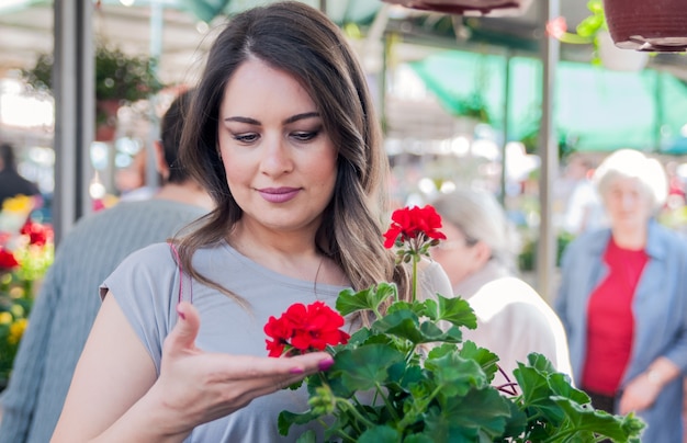 Young woman holding geranium in clay pot at garden center. Gardening, planting - woman with geranium flowers