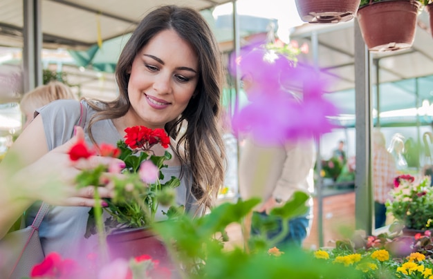 Young woman holding geranium in clay pot at garden center. Young woman shopping flowers at market garden centre