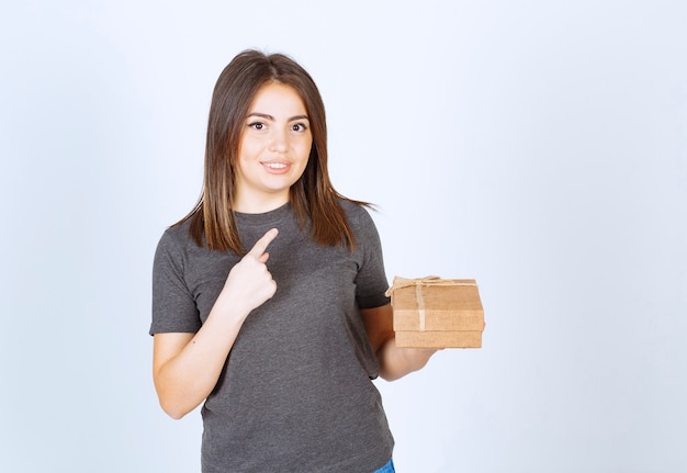 молодая женщина держит подарочную коробку и указывая указательным пальцем.