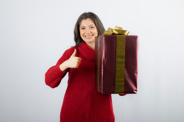 A young woman holding gift box and showing a thumb up. 