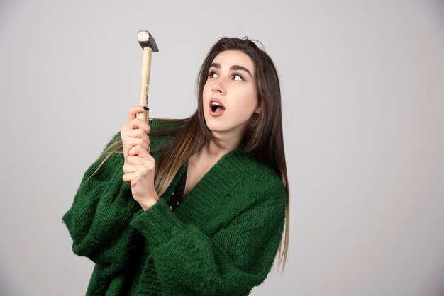 Young woman holding hammer in hands on a gray background.