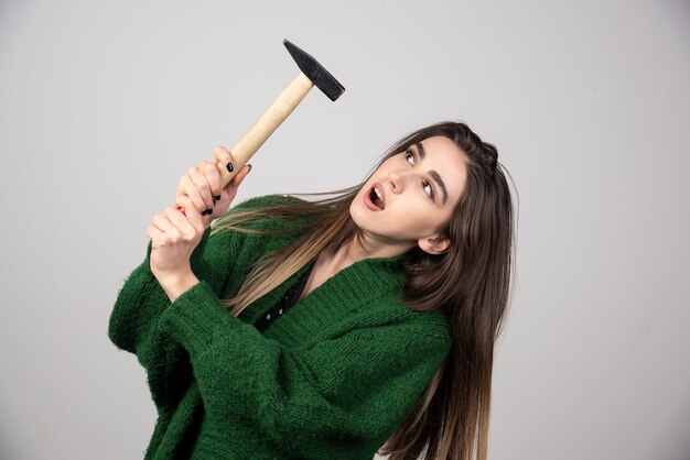 Free photo young woman holding hammer in hands on a gray background.