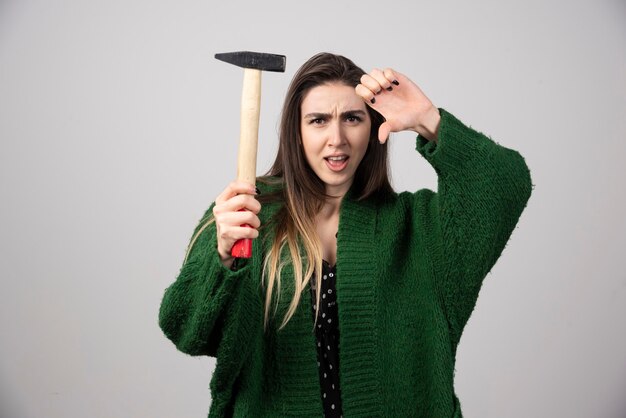 A young woman holding a hammer and showing a thumb down.