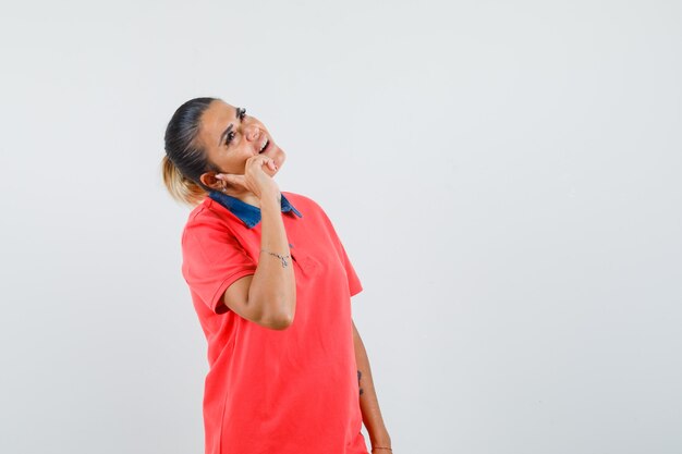 Young woman holding hand as talking on phone in red t-shirt and glasses and looking pensive. front view.