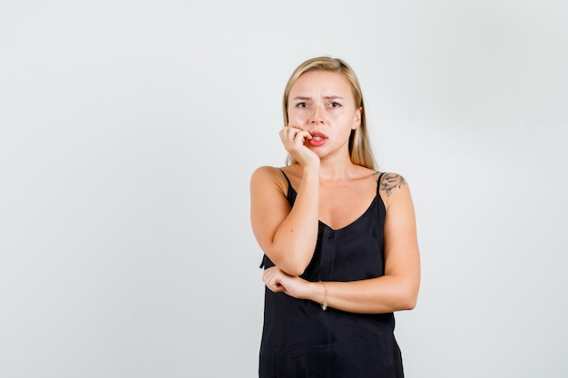 Young woman holding hand on cheek in black singlet and looking worried.