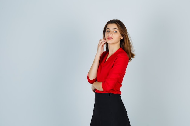 Young woman holding hand on cheek while posing in red blouse