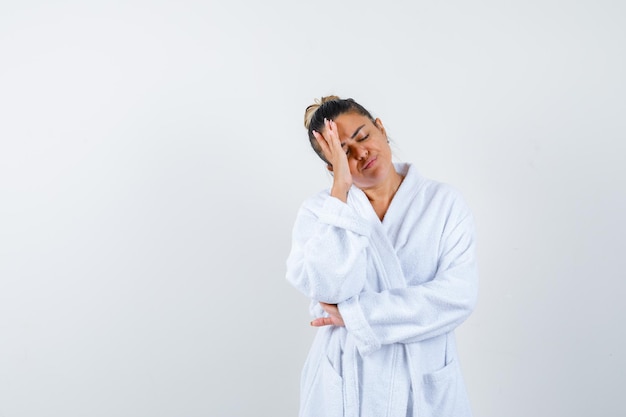 Young woman holding hand on face in bathrobe and looking thoughtful