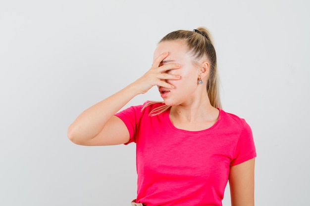 Young woman holding hand on face in t-shirt and looking distressed