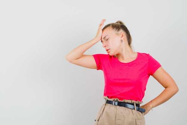 Young woman holding hand on forehead in t-shirt and pants and looking depressed