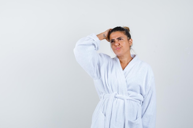 Young woman holding hand on head in bathrobe and looking confident