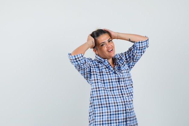 Young woman holding hand on head in checkered shirt and looking gratifying.