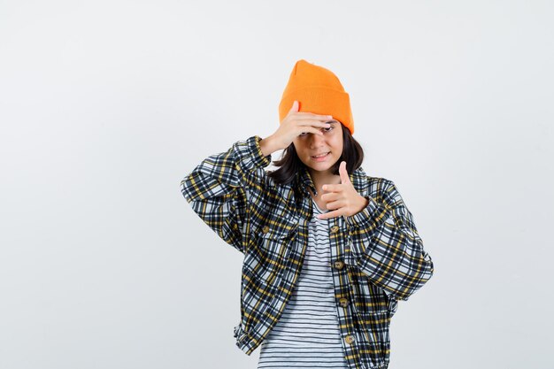 Young woman holding hand on head in orange hat and checkered shirt looking displeased