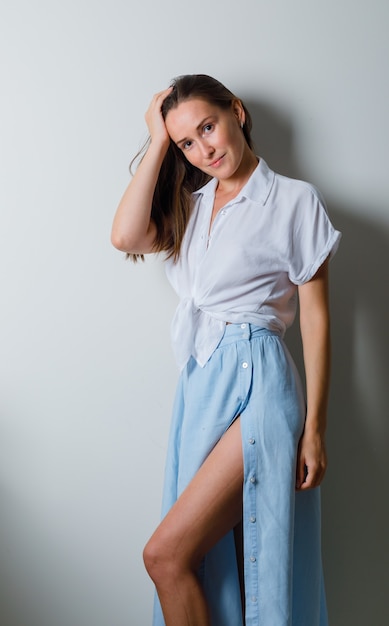 Young woman holding hand on head and posing at front in white t-shirt and light blue skirt and looking charming