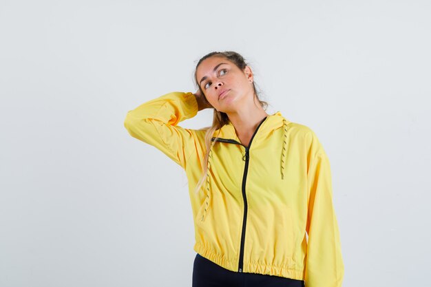 Young woman holding hand on head while looking away in yellow raincoat and looking focused