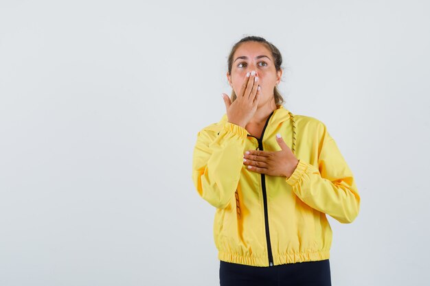 Free photo young woman holding hand on her mouth in yellow raincoat and looking scared