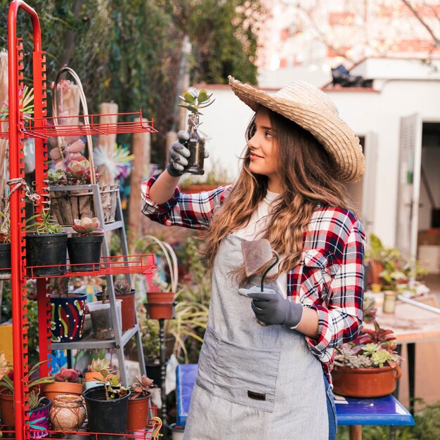 庭でサボテンの植物を見て手で鍬を保持している若い女性