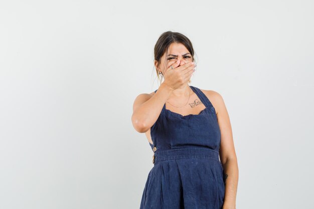 Young woman holding hand on mouth in dress and looking disgusted