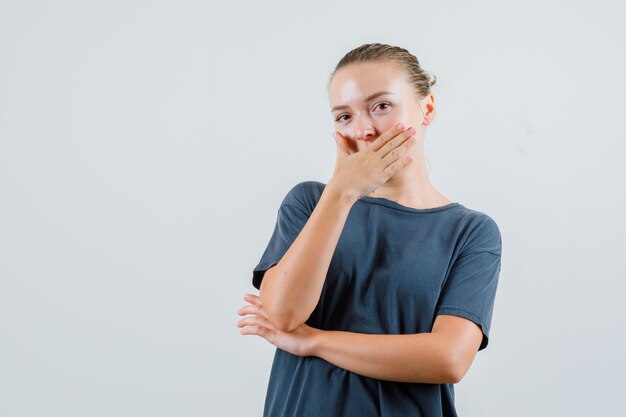 灰色のTシャツで口に手をつないで恥ずかしそうに見える若い女性