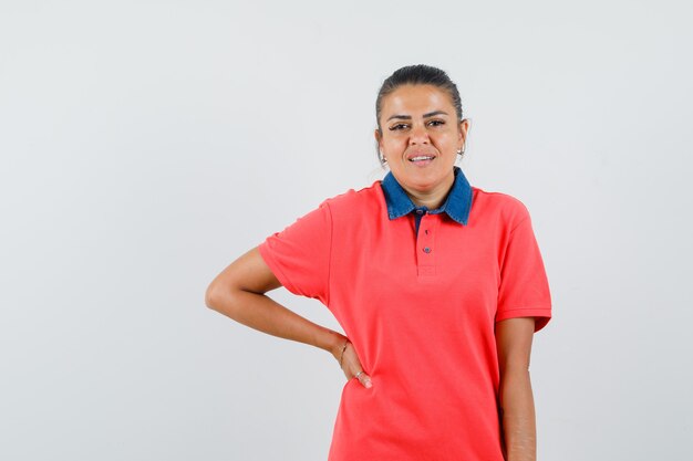 Young woman holding hand on waist in red t-shirt and looking pretty , front view.