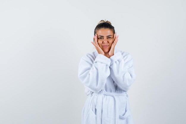 Young woman holding hands on cheeks in bathrobe and looking confident