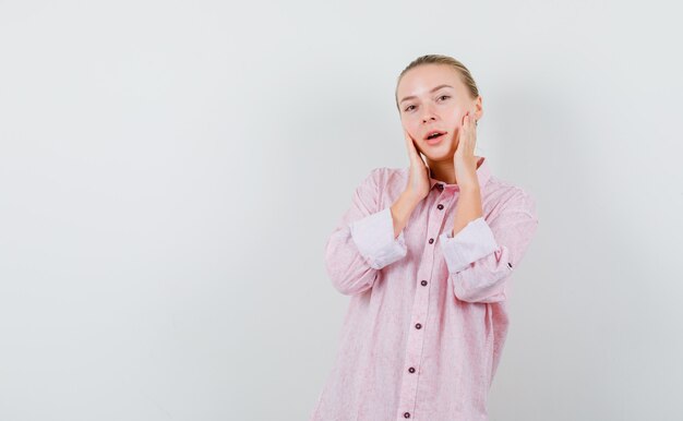 Young woman holding hands on cheeks in pink shirt and looking fresh