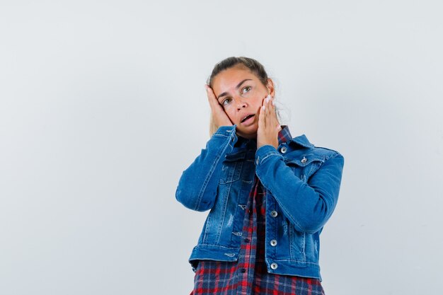 Young woman holding hands on cheeks in shirt, jacket and looking tempting. front view.