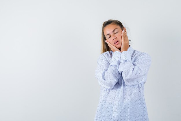 Young woman holding hands on cheeks in white shirt and looking tired