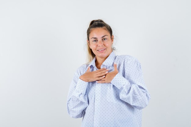 Young woman holding hands over chest in white shirt and looking cheerful