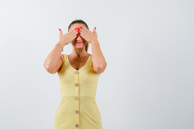 Giovane donna che tiene le mani sugli occhi in abito giallo e guardando vergogna, vista frontale.