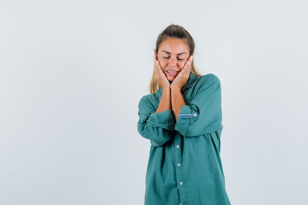 Young woman holding hands on face in green blouse and looking happy