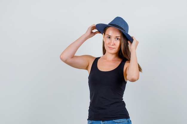 Молодая женщина, взявшись за руки на шляпе и улыбаясь в синглет, вид спереди шорты.