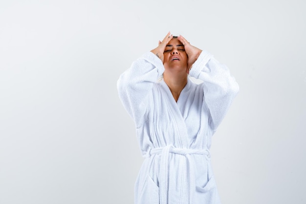 Young woman holding hands on head in bathrobe and looking annoyed