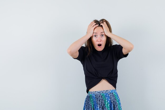 Young woman holding hands on head in black t-shirt and blue skirt and looking annoyed