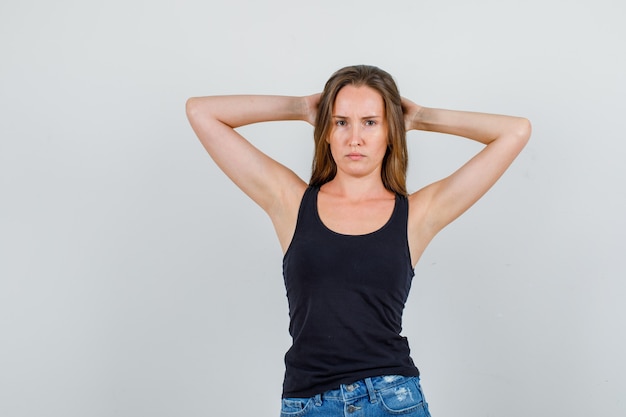 Young woman holding hands behind head in singlet, shorts and looking sad