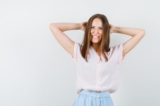 Young woman holding hands behind head in t-shirt, skirt and looking crazy , front view.