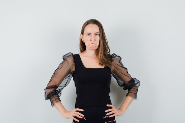 Young woman holding hands on her waist in black blouse and looking frenetic 