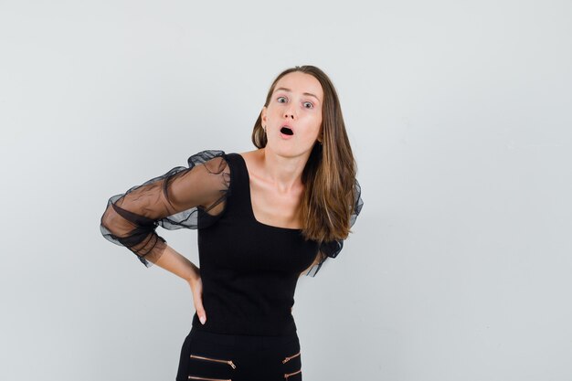 Young woman holding hands on her waist in black blouse and looking troubled 