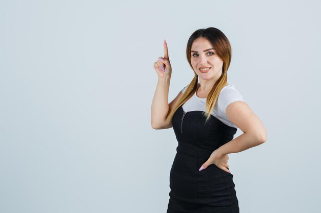 Young woman holding hands on hip and pointing index finger in eureka gesture